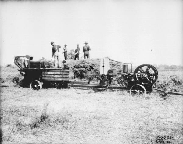 Group of men working with a hay press in a field.