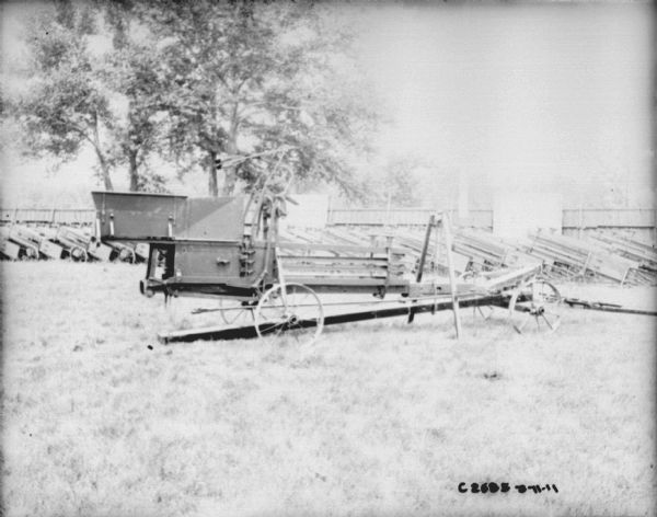 View of hay press in a yard at Springfield Works. A row of other hay presses are in a row near a fence in the background.