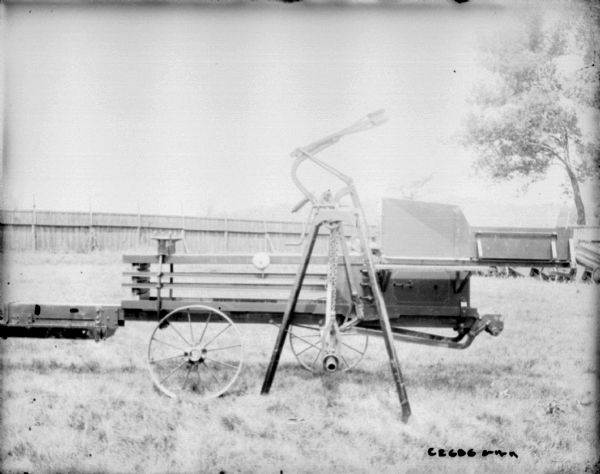 Side view of hay press outdoors at Champion Works. There is a fence in the background and more hay presses.