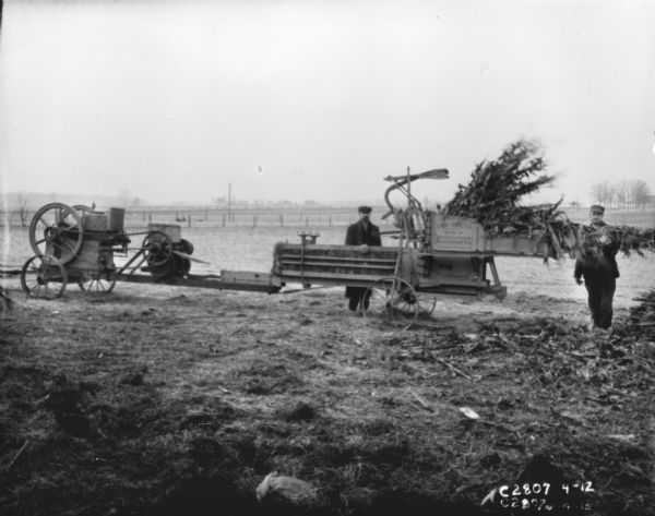 Men baling cornstalks in a field with a hay press.