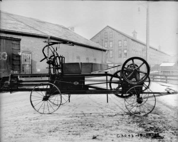 Powered hay press outdoors. There are factory buildings in the background.