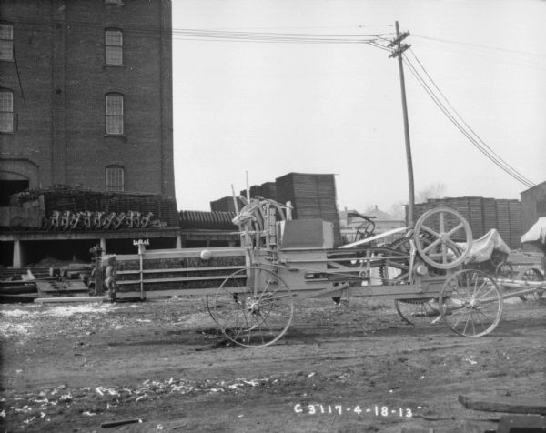 Hay press outdoors. Hay bales are in the hay press. In the background is a loading dock near a factory building.