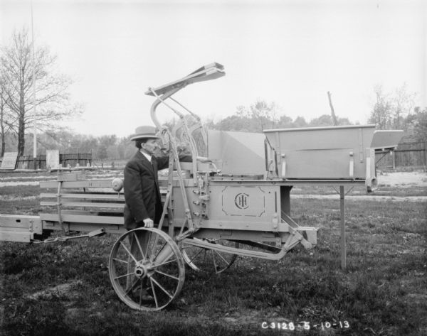 Man posing outdoors with IHC hay press. In the background is a fence and billboards.