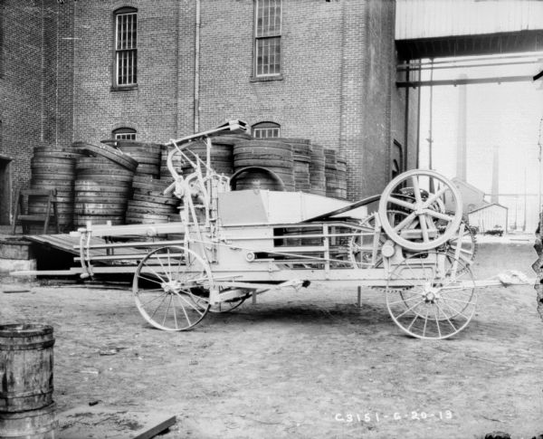 Hay press near factory buildings. Wheels are stacked in the background.