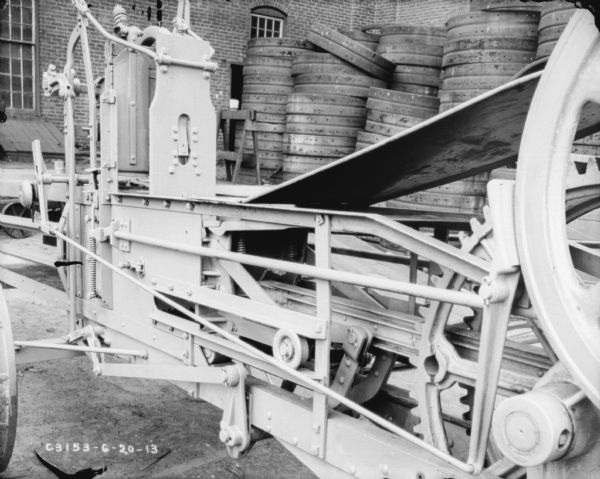 Close-up of hay press outdoors. Wheels are stacked in the background near the side of a brick factory building.
