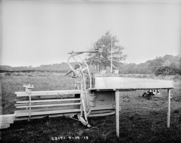 Hay press outdoors in field. In the background is a fence.