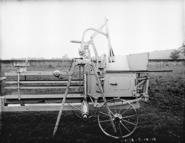 Hay press in field. There is a fence in the background.