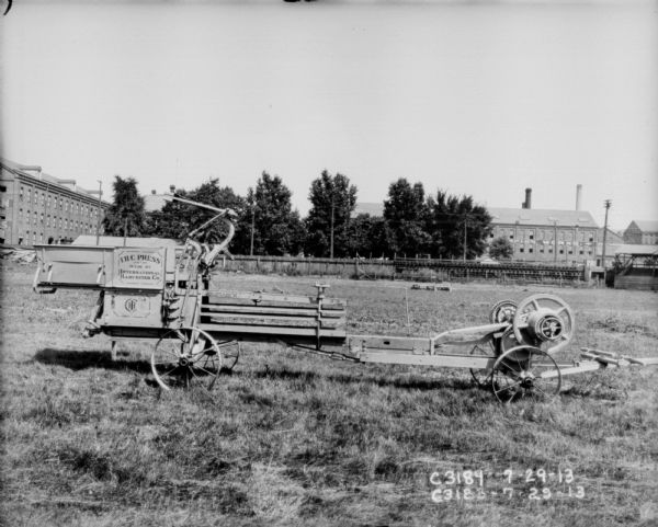 IHC hay press in yard. In the background is a fence and factory buildings. One of the factory buildings has a sign that reads: "Champion Works."