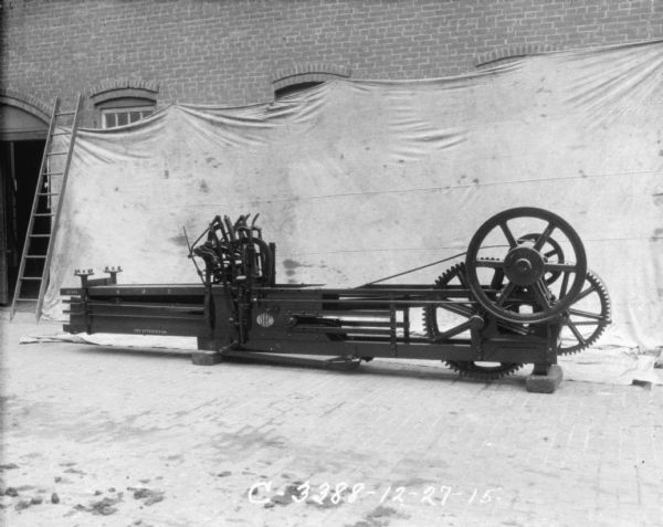 Powered press set up outdoors in front of a backdrop against the side of a brick factory wall.