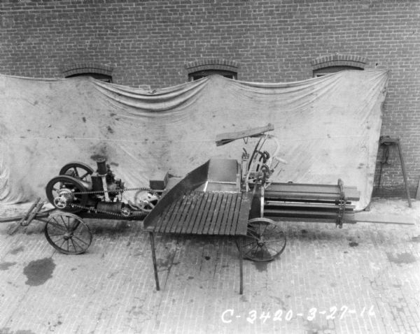 Elevated view of powered hay press in front of a backdrop against a brick factory wall.