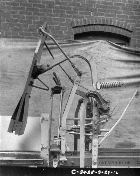 Section of hay press in front of a backdrop against a brick factory wall.