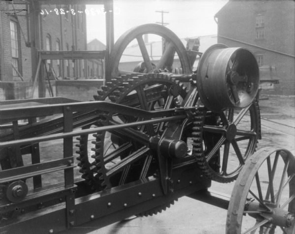 Close-up of powered hay press outdoors. Factory buildings are in the background.
