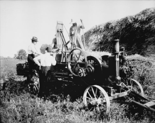 Men working in a field using a powered hay press.