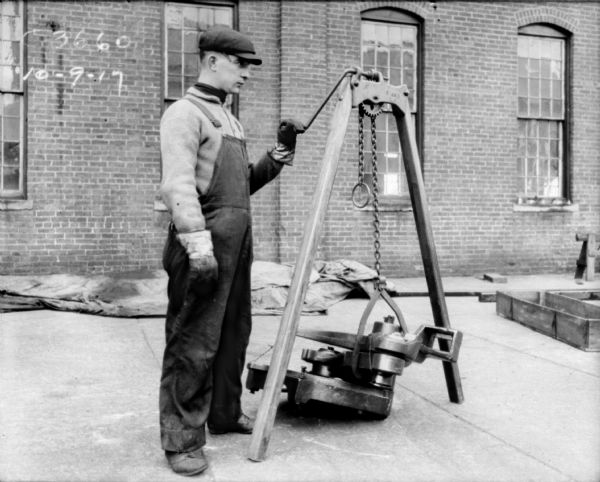 Man standing outdoors at Champion Works. He is holding onto the handle of a lifting jack which is attached to a heavy machine part sitting on the ground.