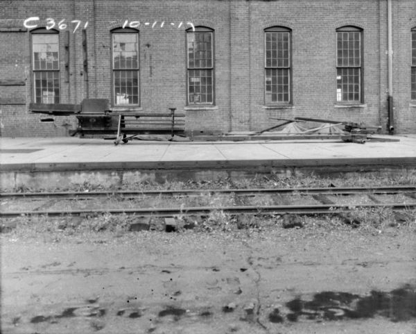 View across railroad tracks towards a hay press on a loading dock in front of brick factory building.