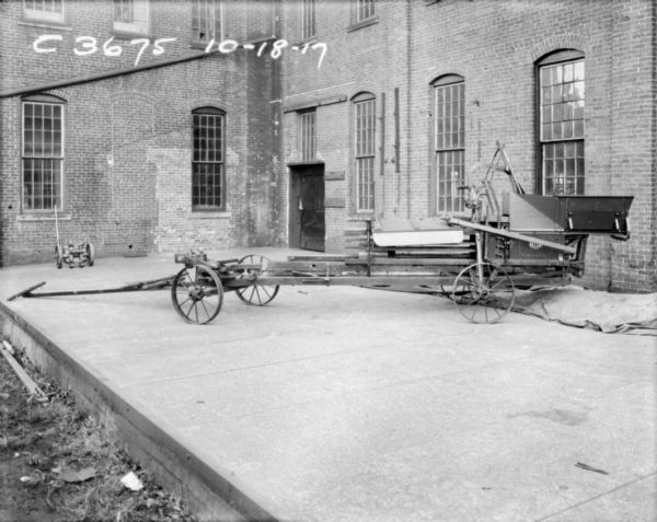 Hay press set up outdoors on a loading dock near a brick factory building.