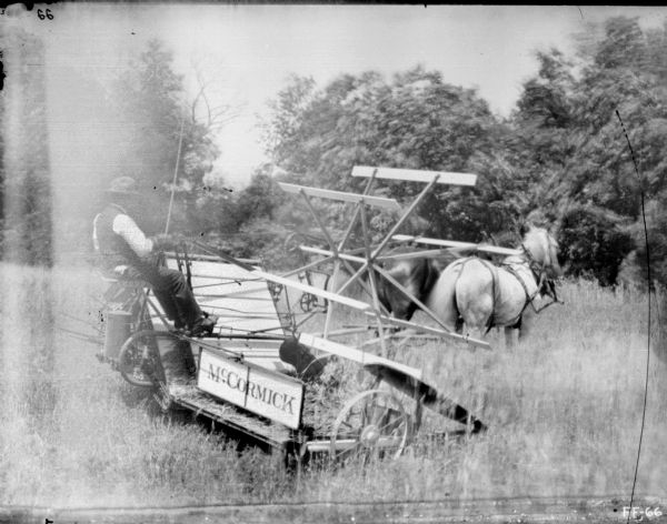 Right side view of a man using a horse-drawn McCormick binder in a field.