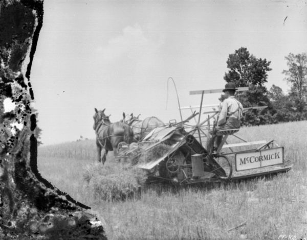 Three-quarter view from left rear of a man using a horse-drawn McCormick mower in a field.