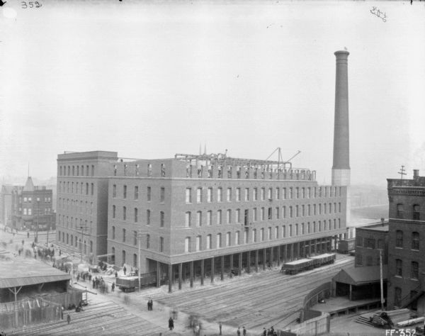 Elevated view of twine mill under construction. Men are standing on and near many sets of railroad tracks. There is a large smokestack on the right.