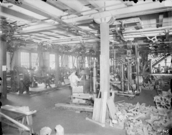 Interior view of men working in machine shop. Belt-driven machinery is attached to the ceiling.