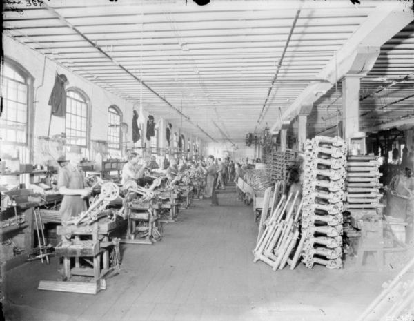 Interior view of men working in the binder attachment room at McCormick Works. The worker's coats and hats are hung up high on the brick wall between the large windows.