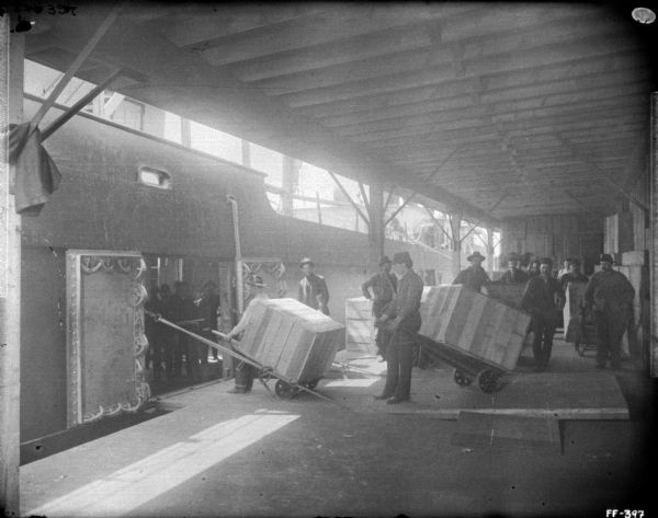 View from roofed loading area of ship at dock. Men are waiting to load crates using hand carts.