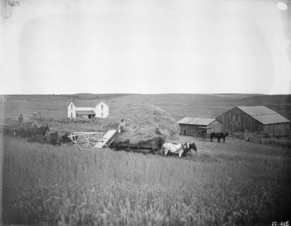View down hill towards men using a horse-powered push binder header. Farm buildings are in the background.