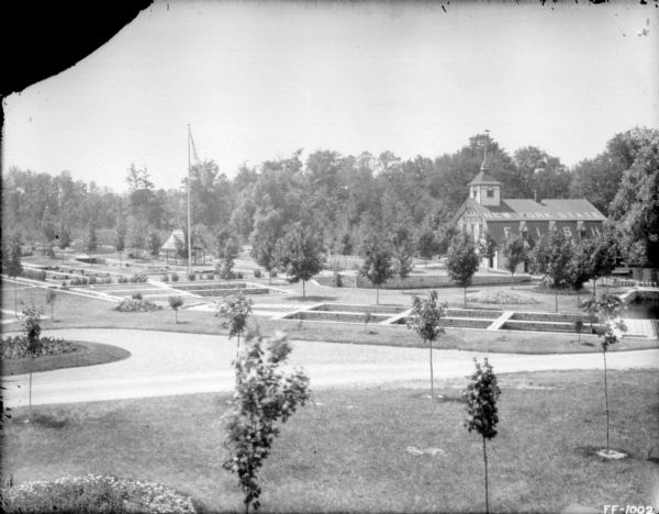 Elevated view across manicured lawns. A flag is on a flagpole on the left. On the far right is a building with a sign on the roof that reads: "New York State," and a sign below along the side: "Fish." There appears to be a fish-shaped wind vane above the cupola on the roof.