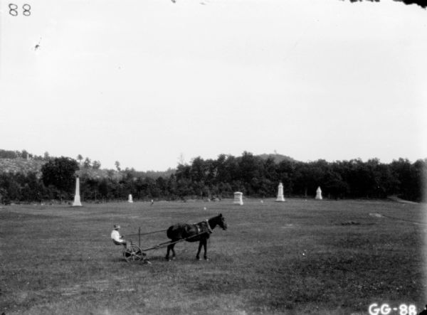 View across lawn towards a man using a mower in a cemetery.