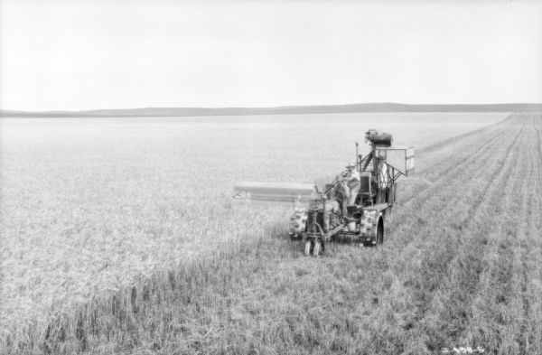 Elevated view of two men on a tractor drawn harvester thresher in a field. Low hills are in the far distance.