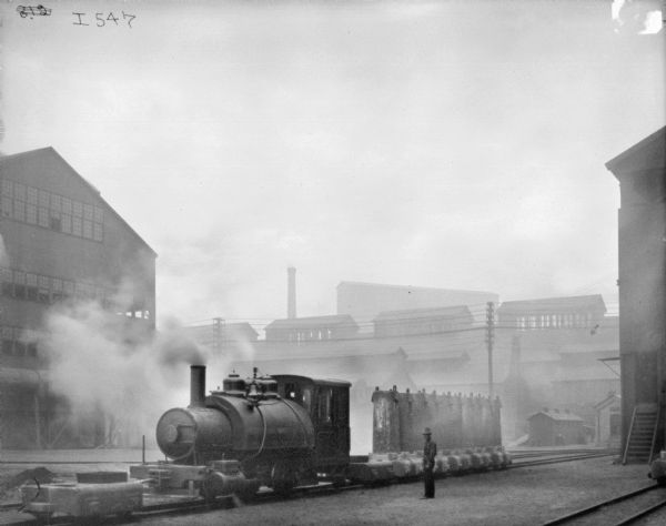 Railroad engine entering plant yard. A man is standing near the tracks.