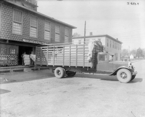 View across road towards two men standing on a loading dock with crates of eggs near the back of a truck. The sign above the loading dock reads: "Missouri Egg & Poultry."