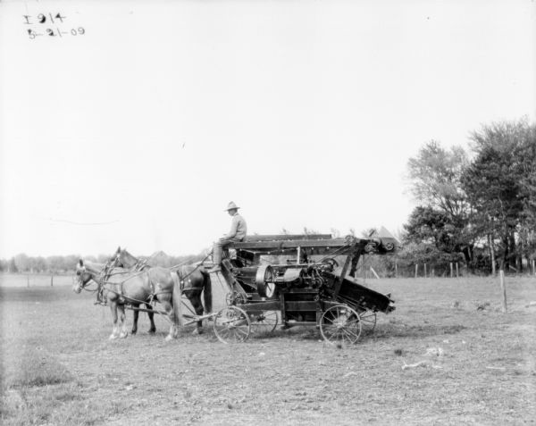 Left side view of a man riding on a horse-drawn separator in a field. Folded for transport.