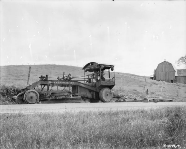 Sawyer-Massey grader for road construction on a road. Farm buildings are in the background.