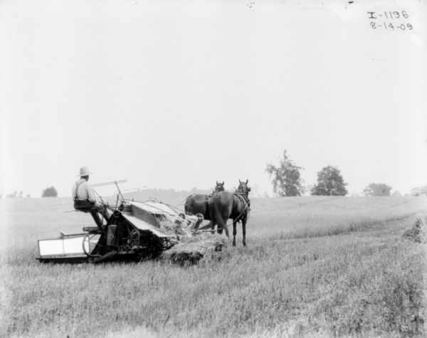 Rear view of a man using a horse-drawn binder in a field.