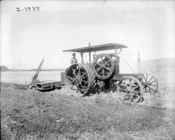 Right side view of a man using a tractor to plow in a field. In the background is a line of power poles.