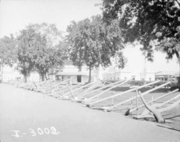 Walking plows lined up outdoors in a long row. Buildings are in the background.