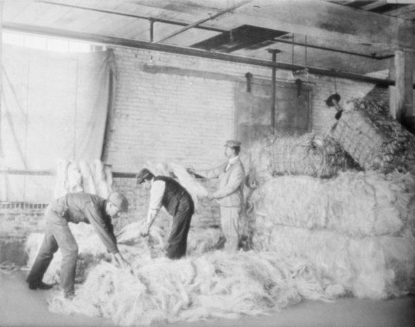 Interior view of three men loading bales of hemp in a warehouse.