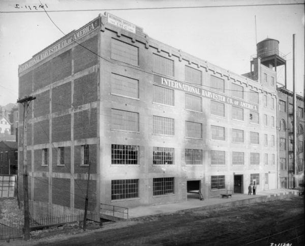 Elevated exterior view of company building. Men are standing on the loading dock. Railroad tracks are in the lower foreground. A water tower is on the roof on the far right.