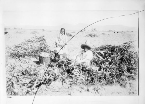 Man (sitting) and a woman (standing) and posing in a field with harvested corn.