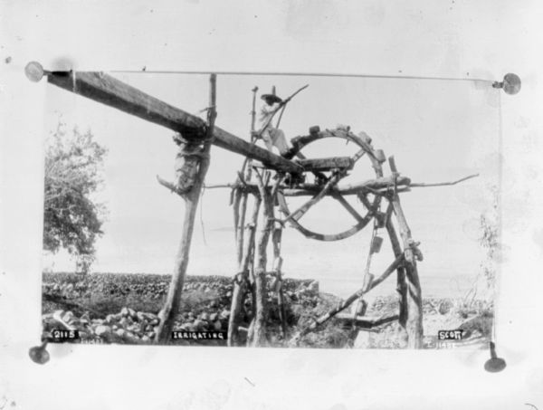 A man is sitting on a water wheel used for irrigation.