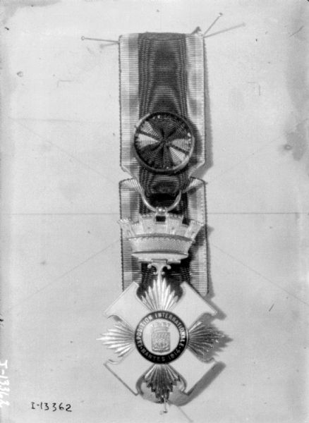 Medal from the Exposition Internationale pinned to a board.