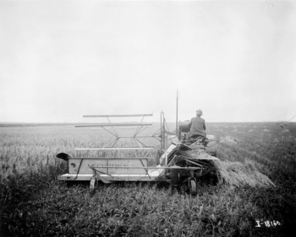 Rear view of a man using a tractor-drawn McCormick binder in a field.