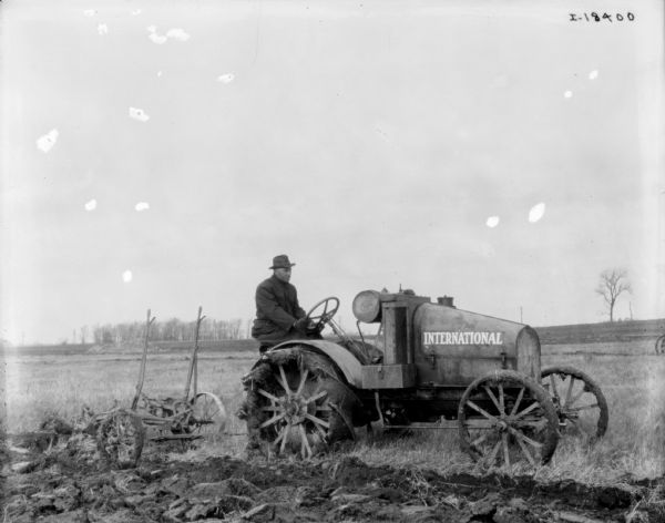 Right side view of man on an International tractor pulling a plow in a field.
