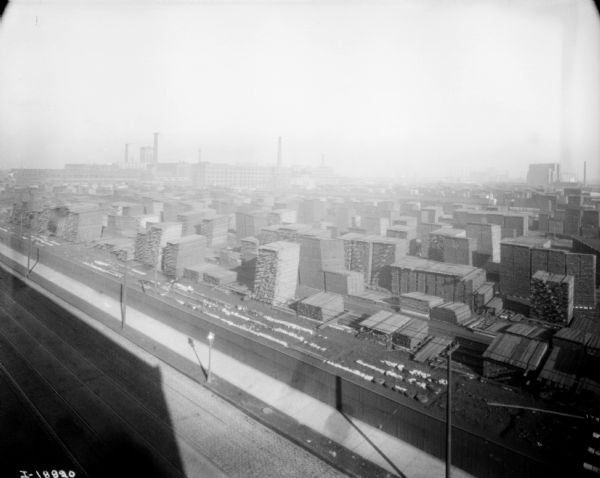 Elevated view of lumberyard at factory. There is a road in the foreground with what appear to be streetcar tracks.