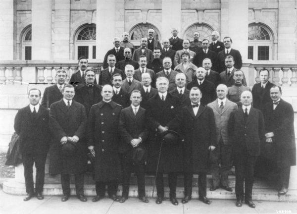 Group portrait of men, and one woman, posing on the steps of a building outdoors.