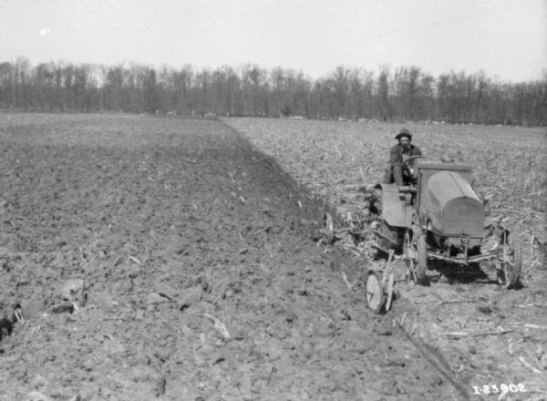 Three-quarter view from front right of a man plowing a field with a tractor.