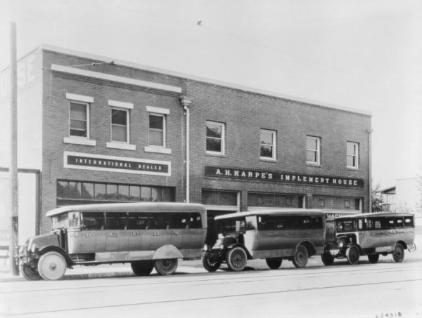 View across street towards three buses in front of an International Dealer storefront and A.H. Karpe's Implement House.
