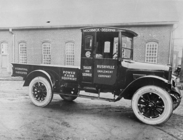 Outdoor view of a truck parked in front of a brick building. Signs painted on the truck reads: "International Harvester," "Power Farm Equipment," "McCormick-Deering," "Sales and Service," and "Rushville Implement Company."