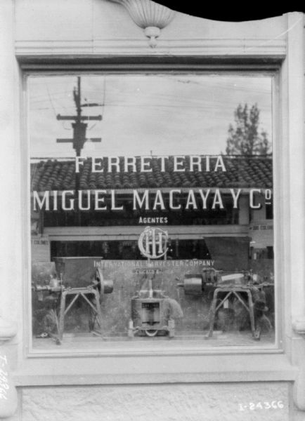 Exterior view of a display window in the facade of a dealership building in Spain. On the window are the words: "Ferreteria Miguel Macaya Y Co. Agentes IHC." Inside the window are what appear to be small-sized versions of various types of equipment.